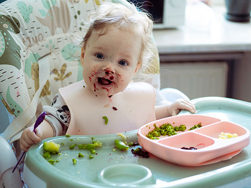 Child in high chair eating green peas.