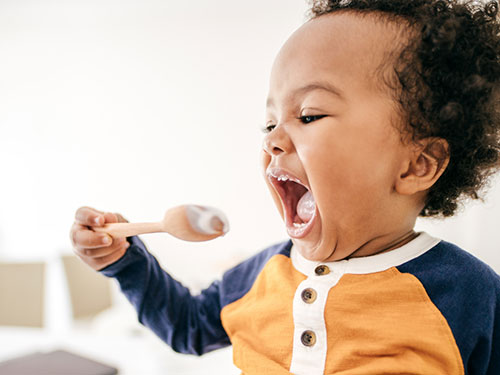 Child in high chair eating vegetables.