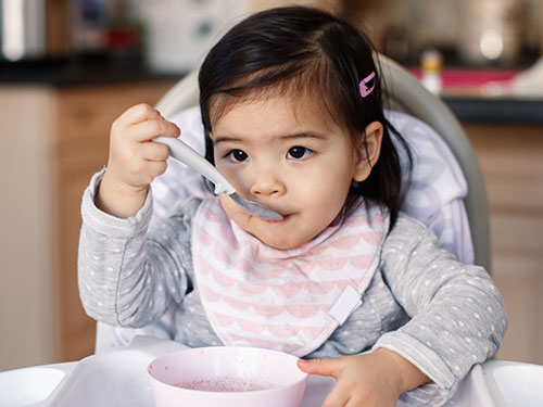 Child sitting in high chair eating carrots and strawberries.