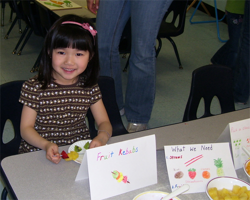 Photo: Girl eating and presenting her fruit kebab.