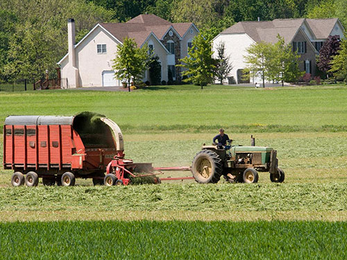 Photo: Tractor and hanger harvesting a farm field near a neighborhood.