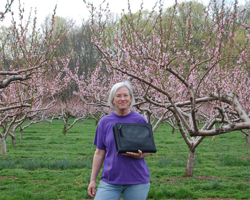 Photo: Farmer in front of trees, holding a briefcase.