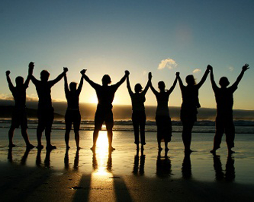 Photo: Group of people holding their hands and raising their arms on a beach.